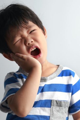 Little Asian boy having toothache, holding his face with hand, dental problem.